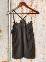 Photo of back of black cami with floral lace detail. Hanging on hanger with tin background