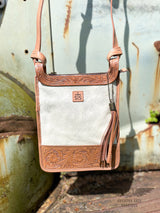 Image of close up of the Yipee Kiyay crossbody purse. The purse has white cowhide front with floral tooled veggie tan leather detail on the top and bottom. STS branded leather patch in the middle of the cowhide and removable decorative leather tassel.